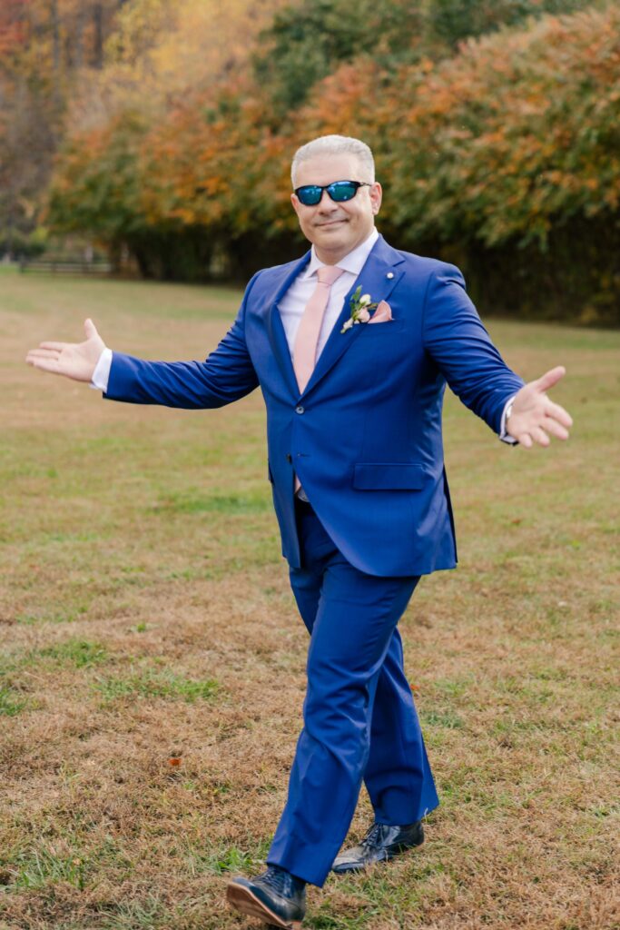 A groom wearing a blue suit cheese at the camera.