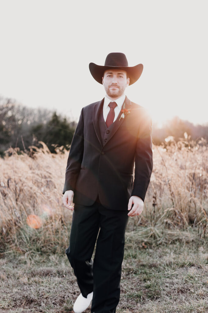 A groom portrait with the sun shining over his shoulder. He wears white sneakers and a black cowboy hat. Wedding venue: 48 Fields Farm. Florist: One Last Avocado Floral Design