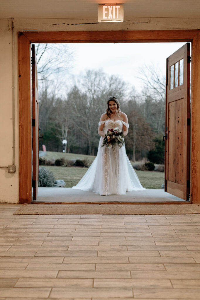 A bride begins walking down the aisle holding a red and white Cascade wedding bouquet. Wedding venue: 48 Fields Farm. Florist: One Last Avocado Floral Design