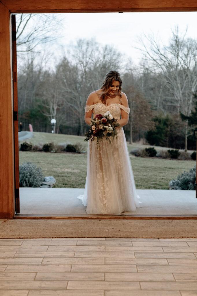 A bride begins walking down the aisle holding a red and white Cascade wedding bouquet. Wedding venue: 48 Fields Farm. Florist: One Last Avocado Floral Design